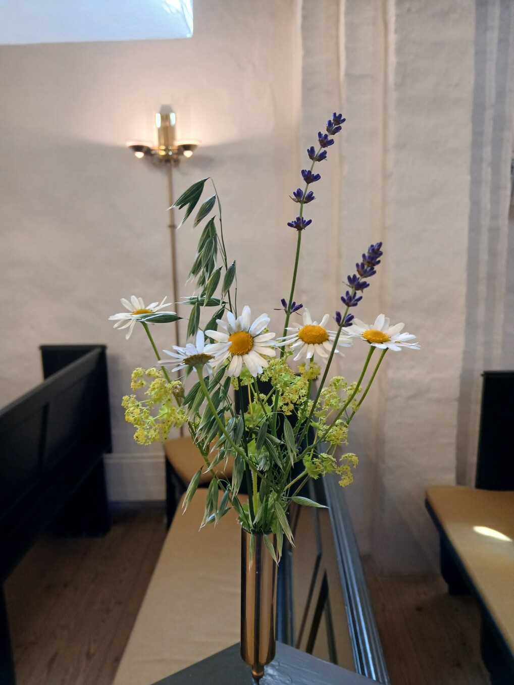 Blomster fra skærehaven i buket i lille vase ved kirkebænkene.